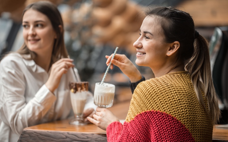 To unge kvinner sitter ved et bord og drikker drikke med sugerør