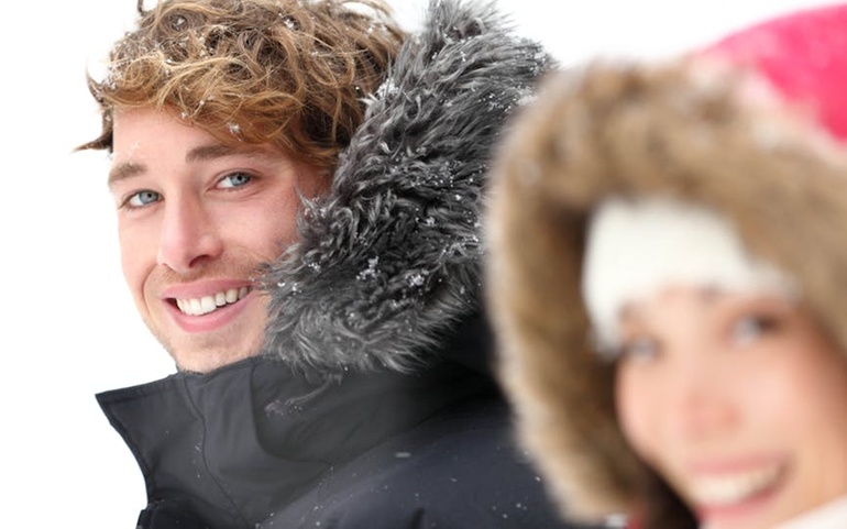 Ung smilende mann med snøfnugg på hår og jakke