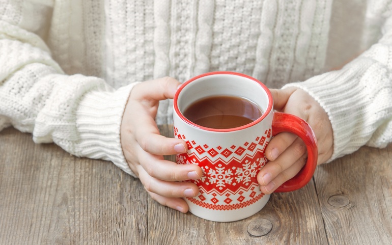Hender holder rundt en kopp varm drikke