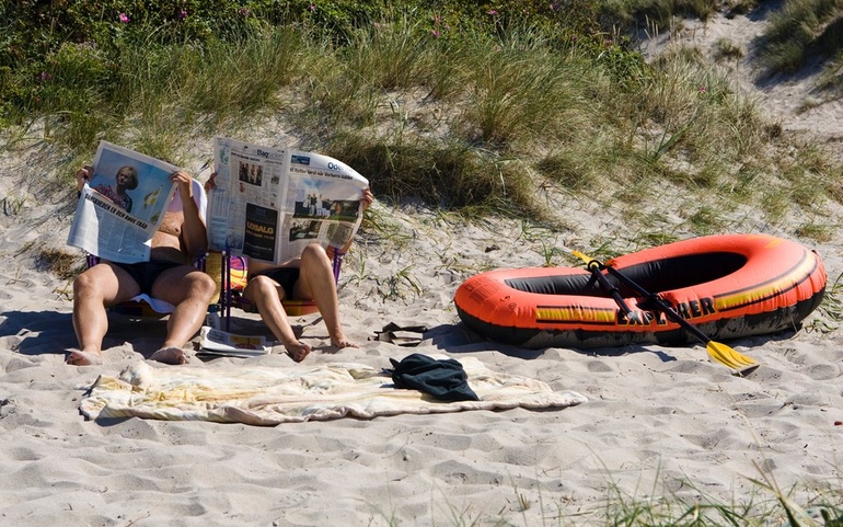 To menn leser aviser på ei strand